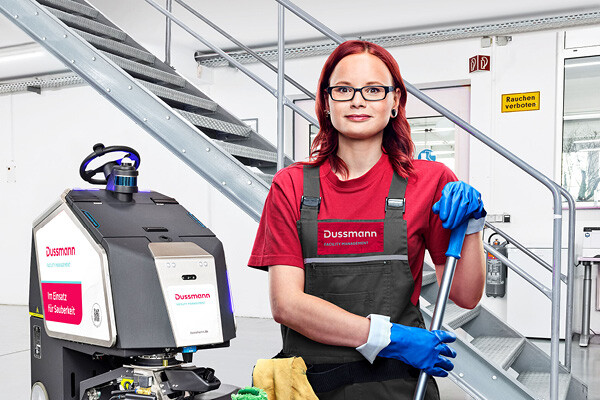 Dussmann trainee holding a mop and smiling into the camera.