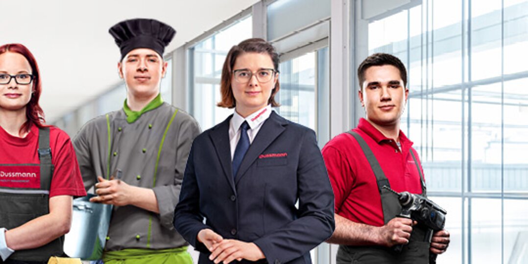 Group picture of 4 smiling Dussmann trainees and students in work clothes from different work areas in front of a white and blue background. 
