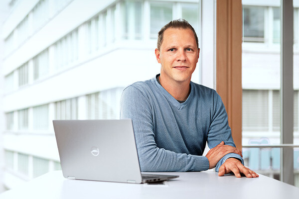 Dussmann employee from the commercial services division, sitting in an office in front of his laptop and smiling. 