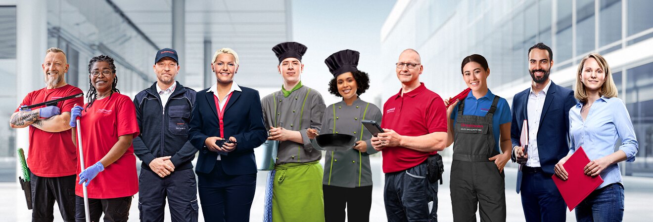 Group picture of smiling Dussmann employees from different work areas in front of a gray background, wearing their work clothes. 