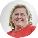 Portrait of a smiling woman with blonde curls and a red T-shirt in front of a grey background 