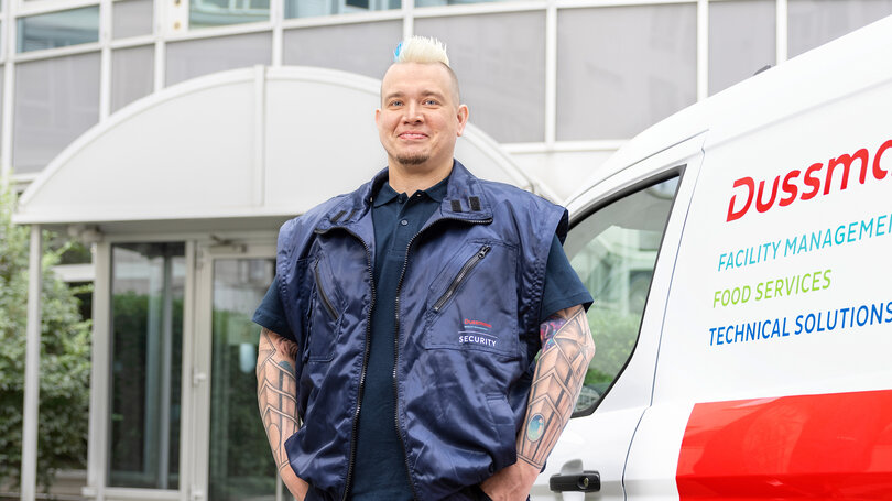 Dussmann - Everyday Professional Maik RIchter Dussmann security guard in uniform standing in front of a Dussmann vehicle